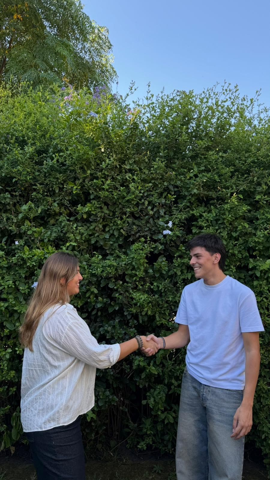 Micaela y Tomás, cofundadores de Pacto, dándose la mano frente a un seto